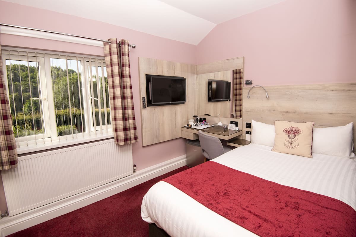 Een hotelkamer met een bed, een bureau met stoel, een aan de muur bevestigde televisie en een raam met gordijnen.