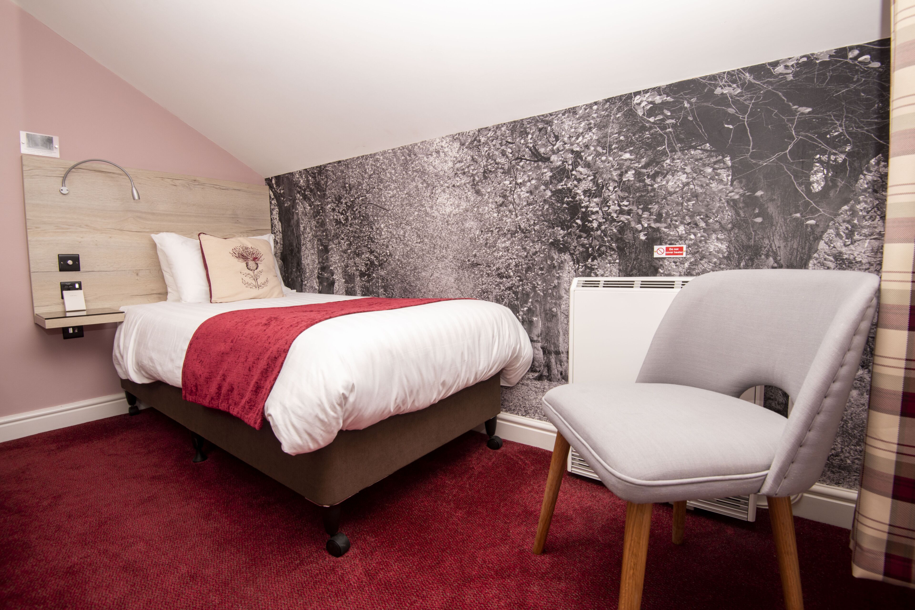 A bedroom with a bed, a chair, a red carpet, a headboard, and a wall with a tree mural.