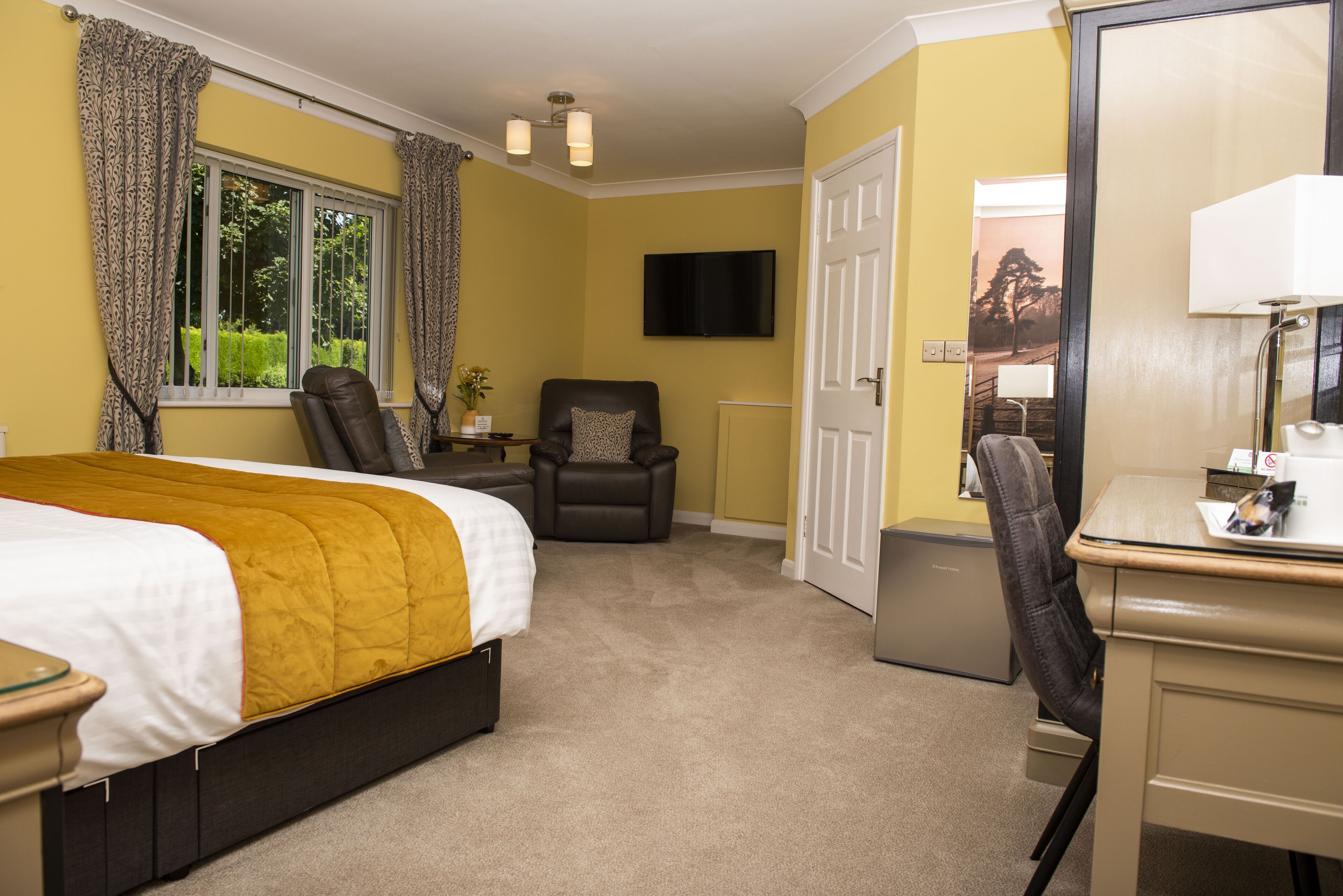 A hotel room with a bed, a desk, a chair, a television, and a door.