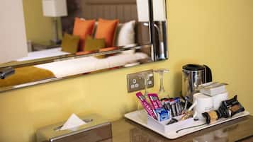 Habitación de hotel con mesita de noche, un espejo, cafetera y una bandeja con aperitivos y caja de pañuelos.