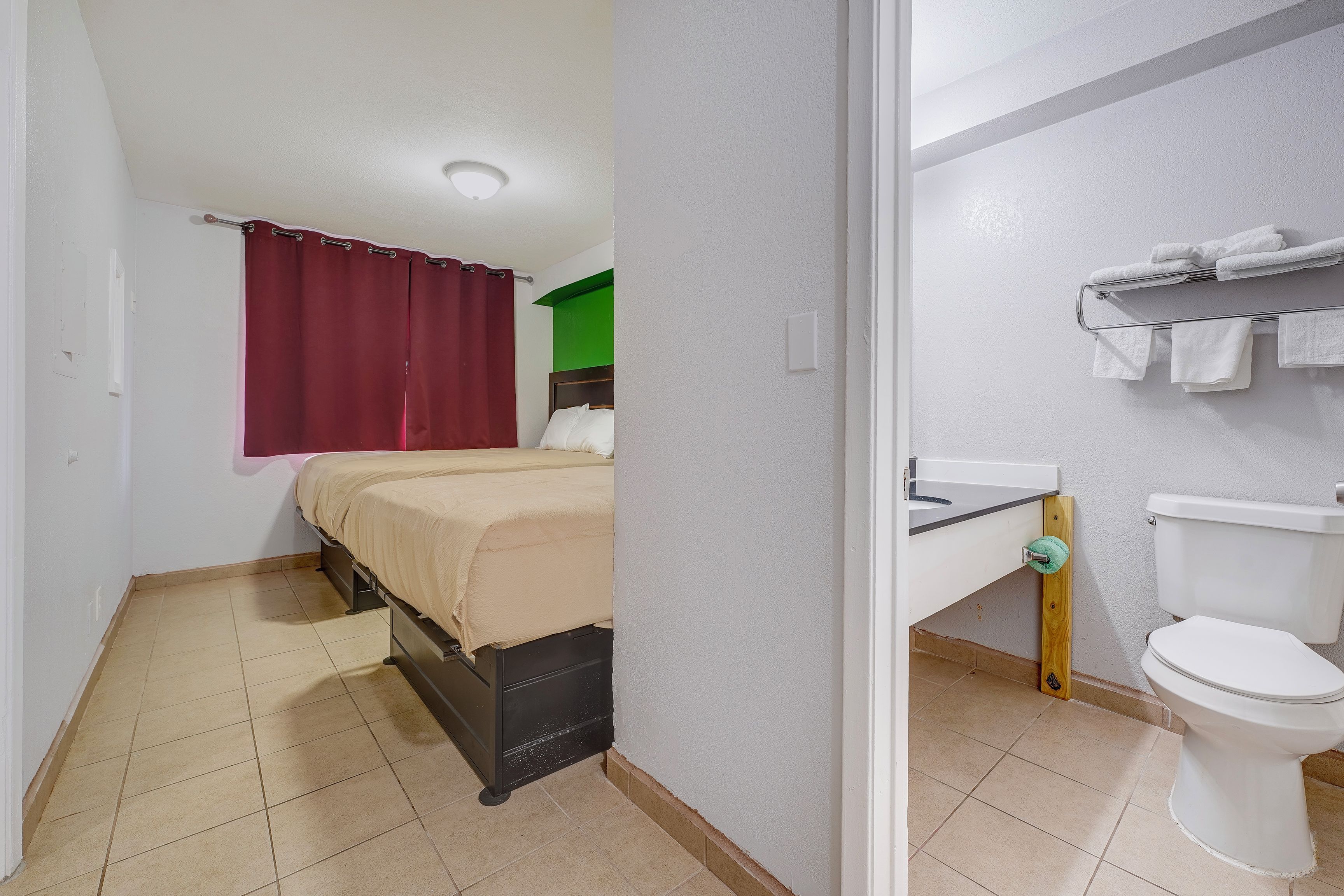 Un dormitorio con cama, un baño con inodoro y cortina de ducha.