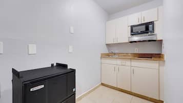 Cocina compacta con armarios blancos, un refrigerador negro y un microondas.