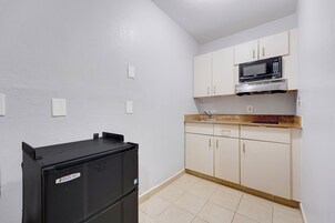 A compact kitchen with white cabinets, a black refrigerator, and a microwave.