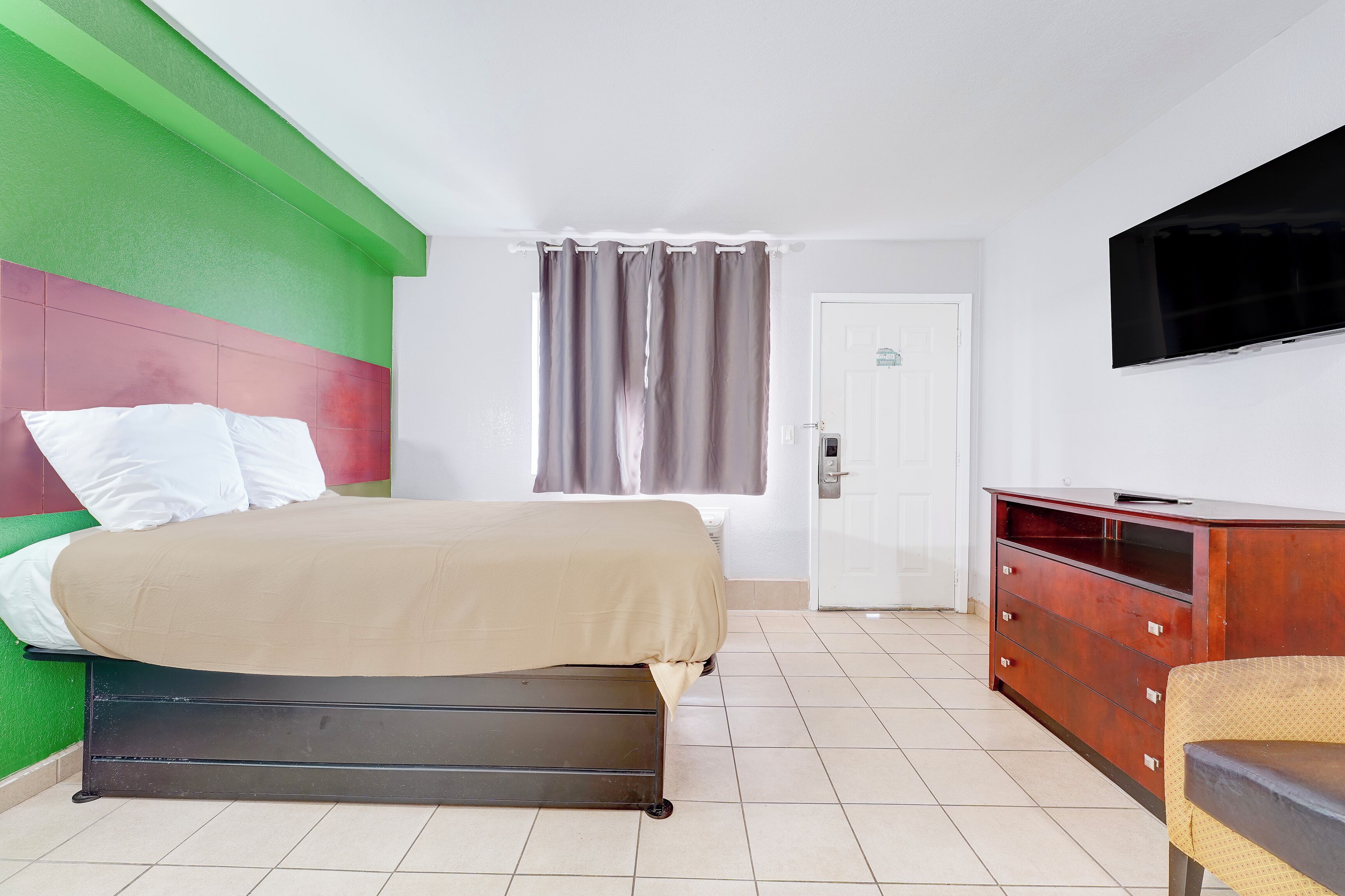 A hotel room with a bed, a television, a dresser, and a door.