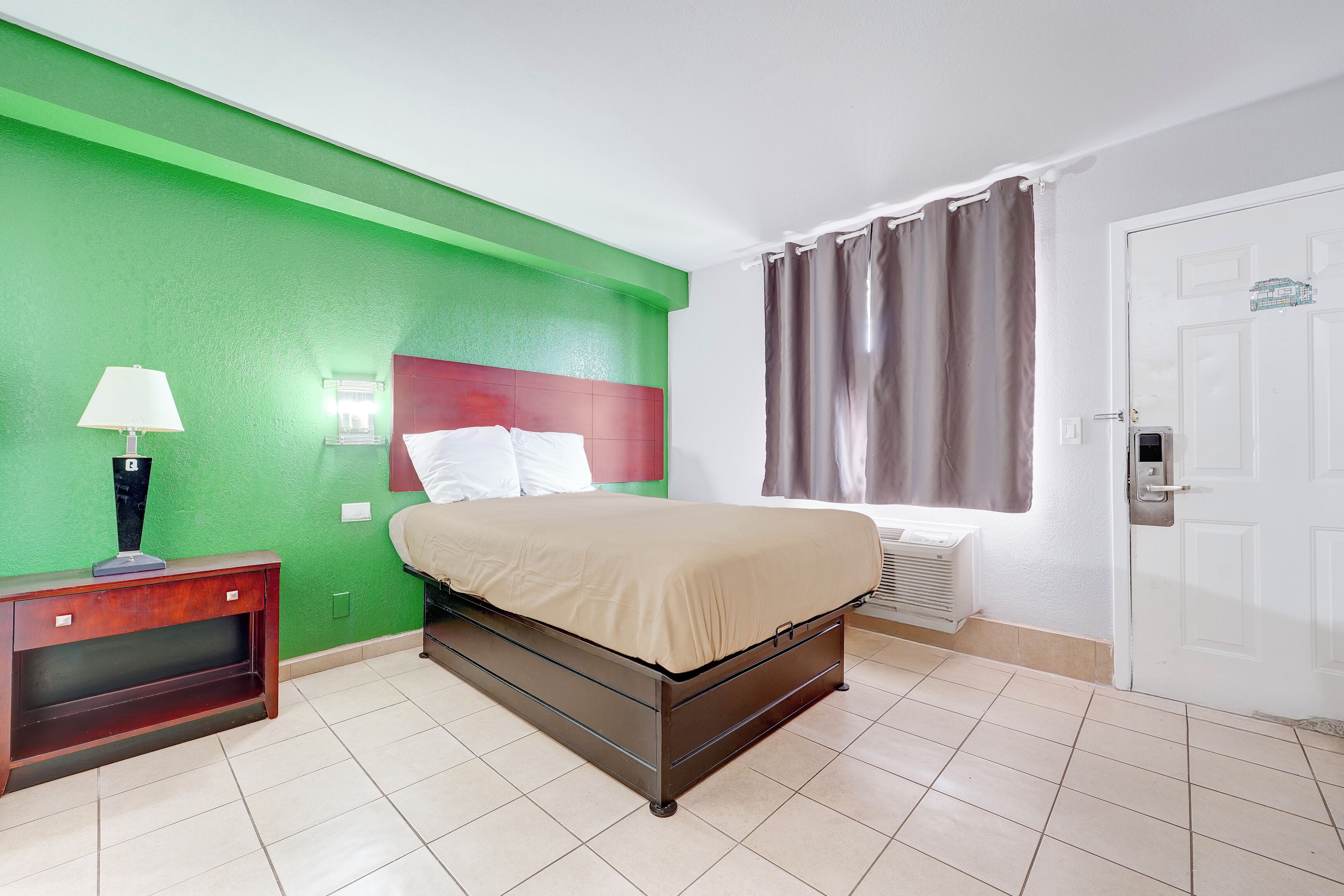 Un dormitorio con cama, mesita de noche, lámpara, ventana con cortinas y puerta.