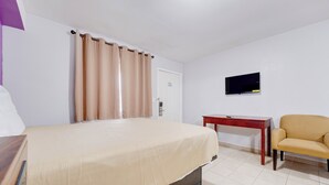A hotel room with a bed, a desk, a chair, a television, and a door.