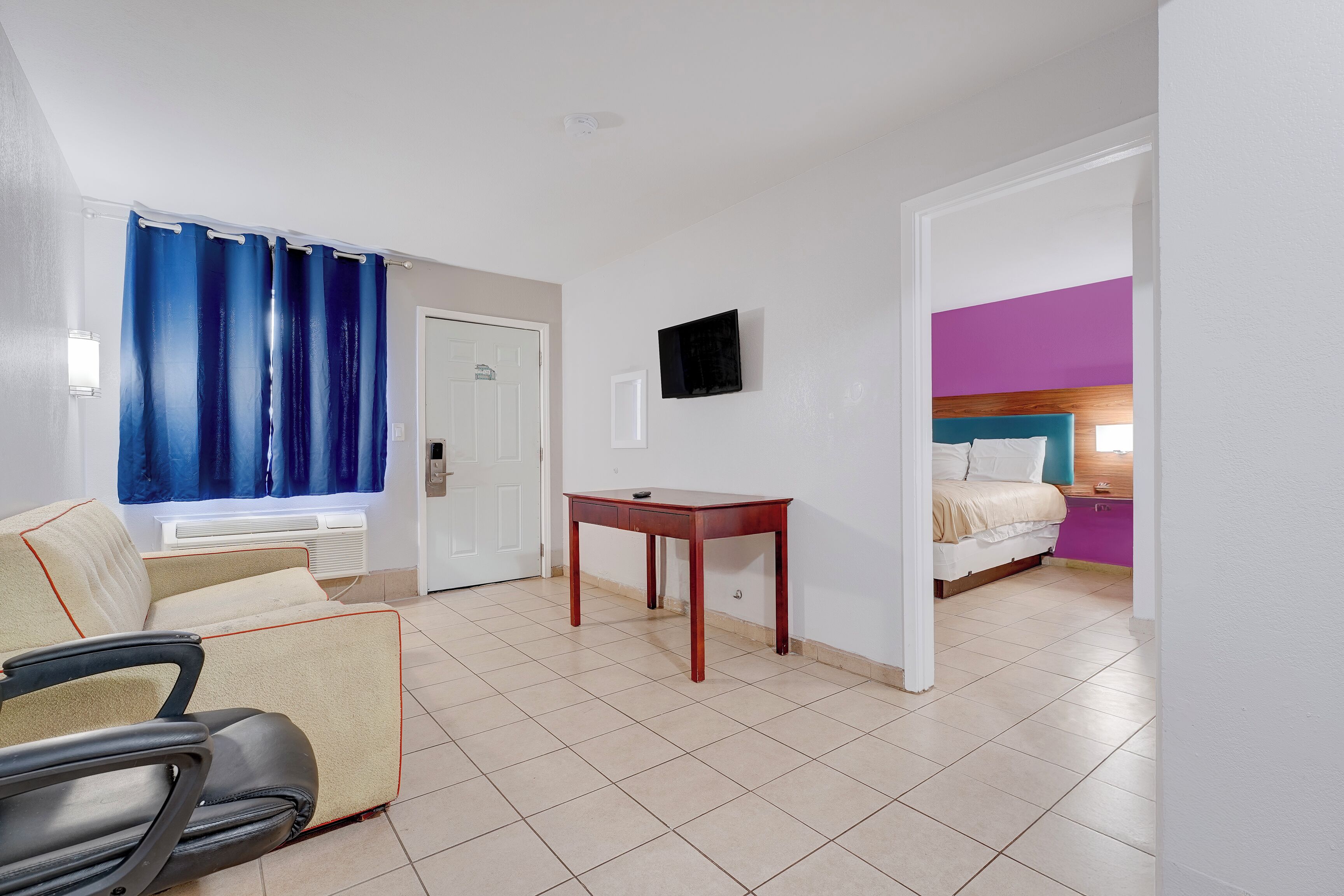 A hotel room with a bed, a desk, a chair, a TV, and a bathroom with a shower curtain.