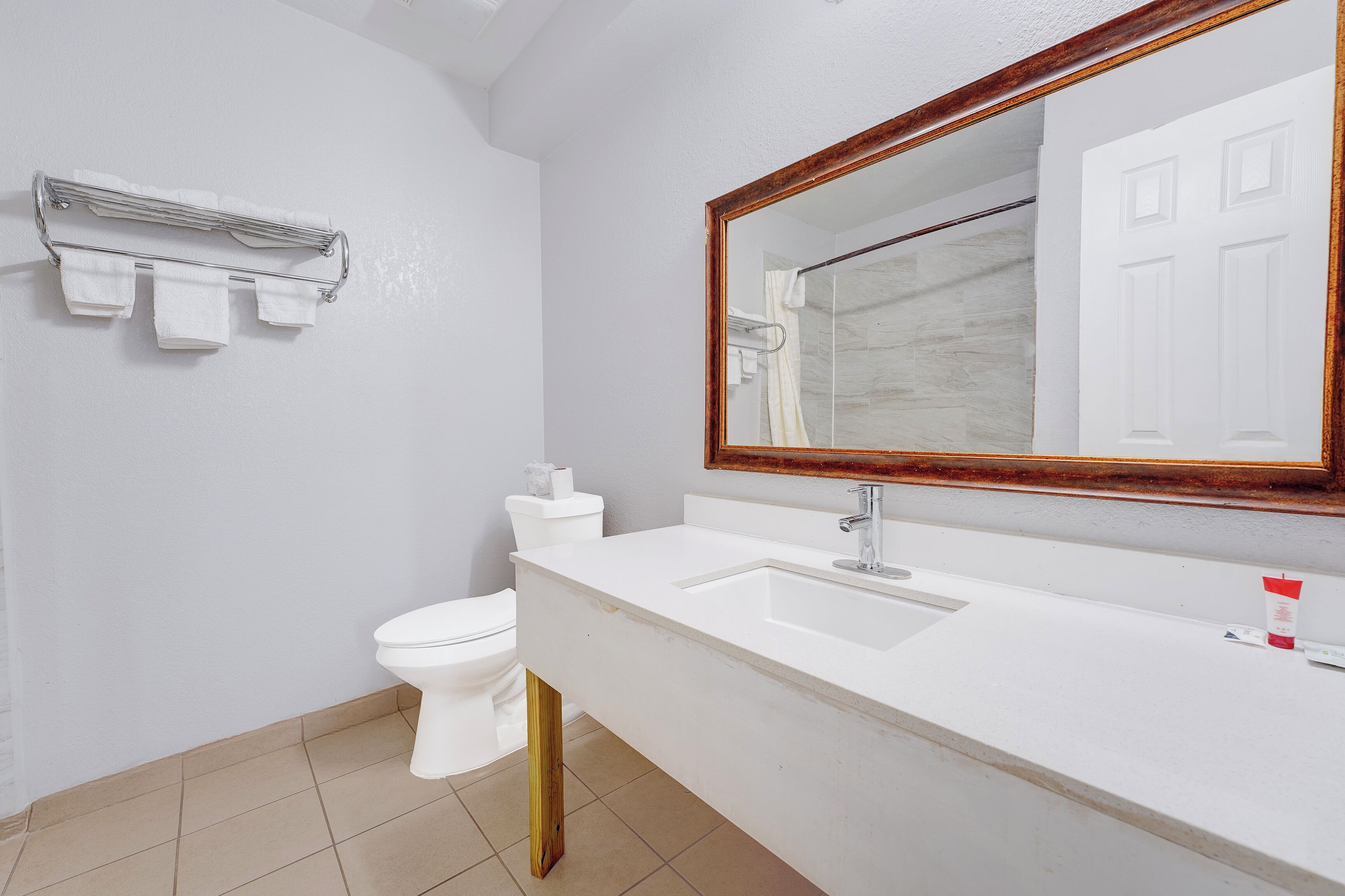 Un baño con un lavamanos blanco, un espejo con marco de madera, un perchero y un inodoro.