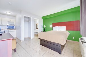 Una habitación con cama, escritorio, kitchenette y pared verde.