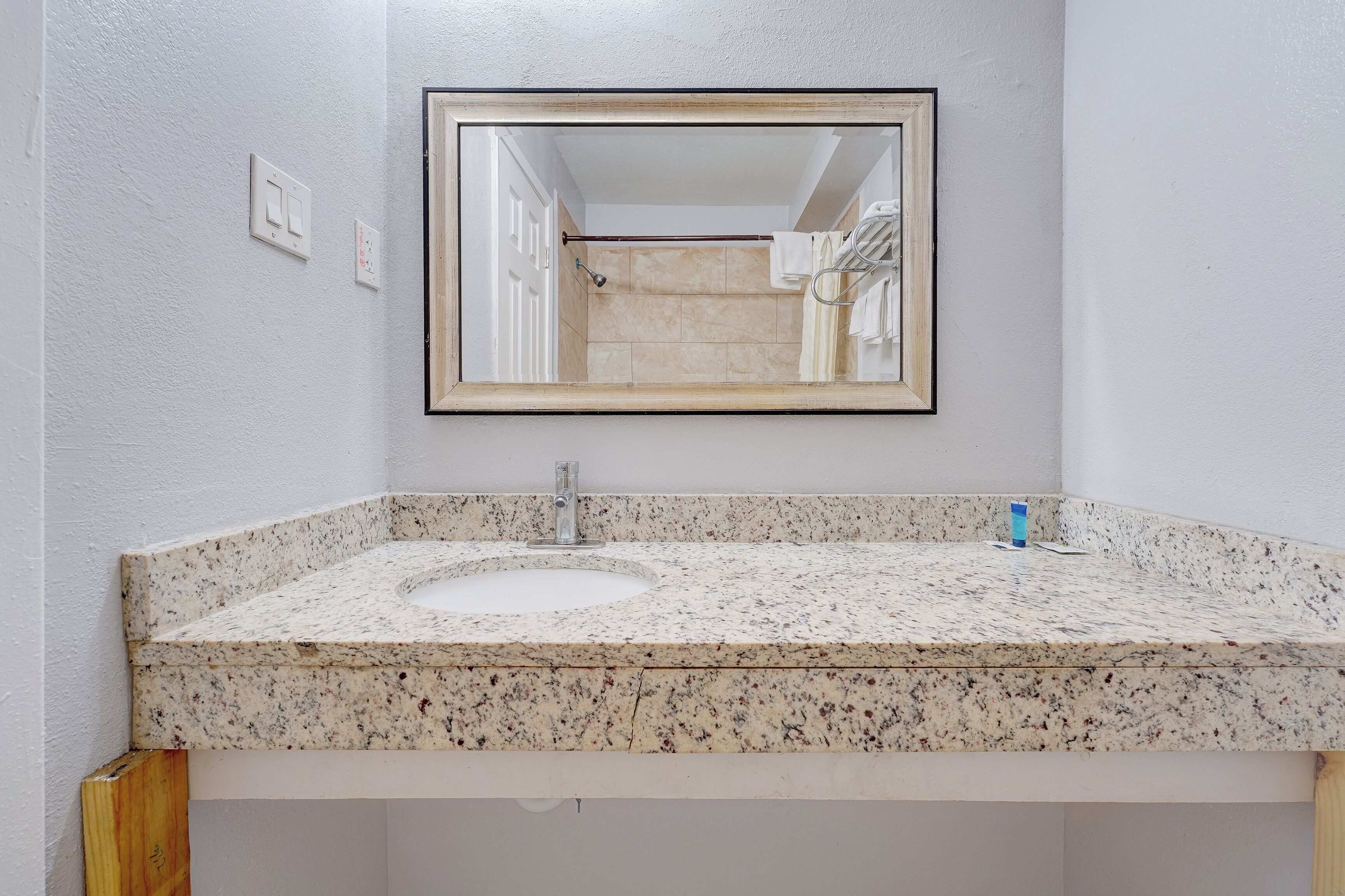 A bathroom with a granite countertop sink, a mirror, and a shower visible in the reflection.