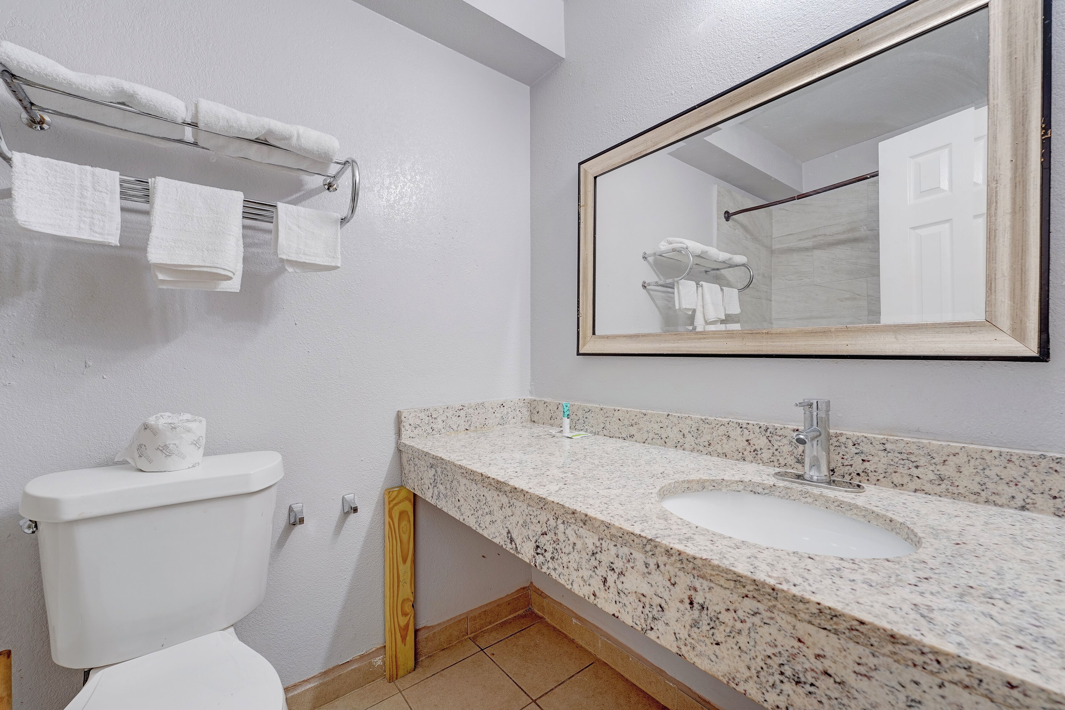 A bathroom with a toilet, a sink, a mirror, and a towel rack.