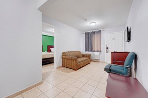 A room with a sofa, a chair, a small table, and a bed.
