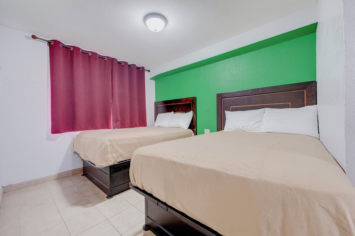 Une chambre avec deux lits, une fenêtre avec des rideaux rouges et un mur vert.