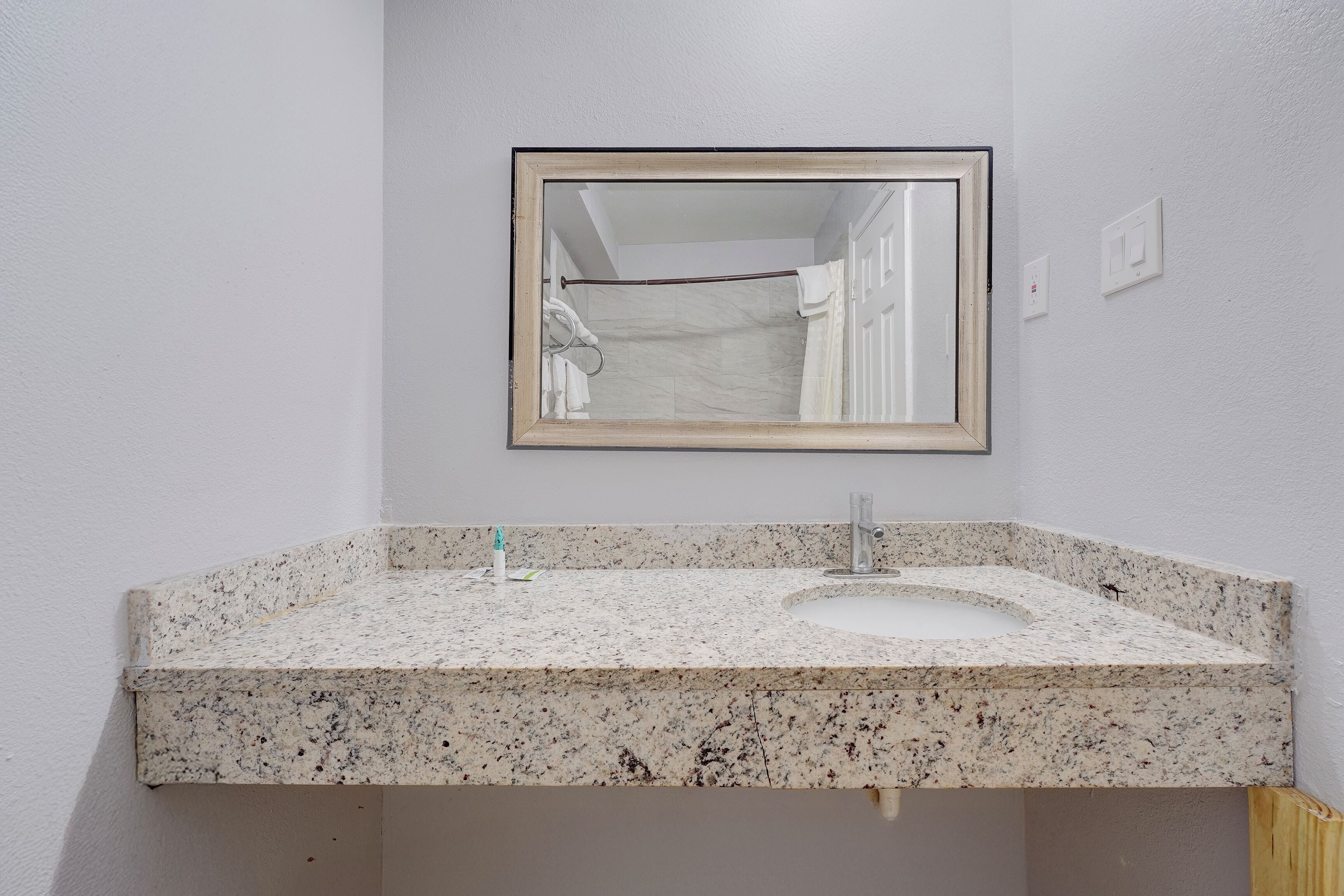 A bathroom with a granite countertop sink, a mirror, and a towel rack.