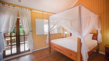 Una cama con dosel de madera y cuatro postes, suelo de madera, balcón con barandilla de madera y pared blanca con ventana.