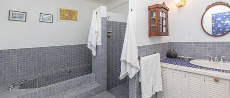Ein Badezimmer mit gefliestem Duschbereich, einem Waschbecken mit dekorativer Seifenschale und einem Spiegel mit ornamentalem Rahmen.