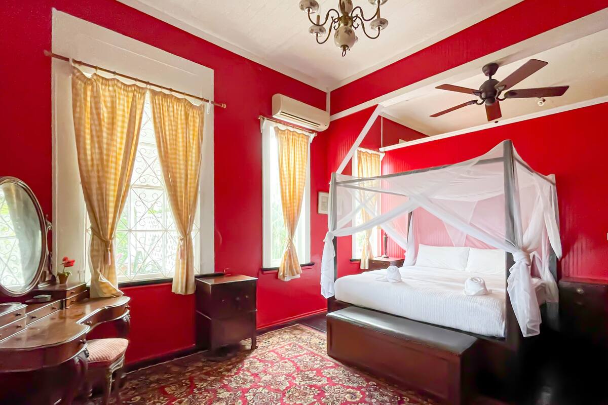 Quarto com cama de dossel, lustre, ventilador de teto e esquema de cores vermelho e branco.
