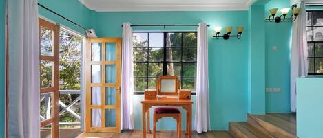 Une pièce aux murs de couleur turquoise, avec un bureau en bois doté d’un miroir, un lit et une fenêtre avec des rideaux.