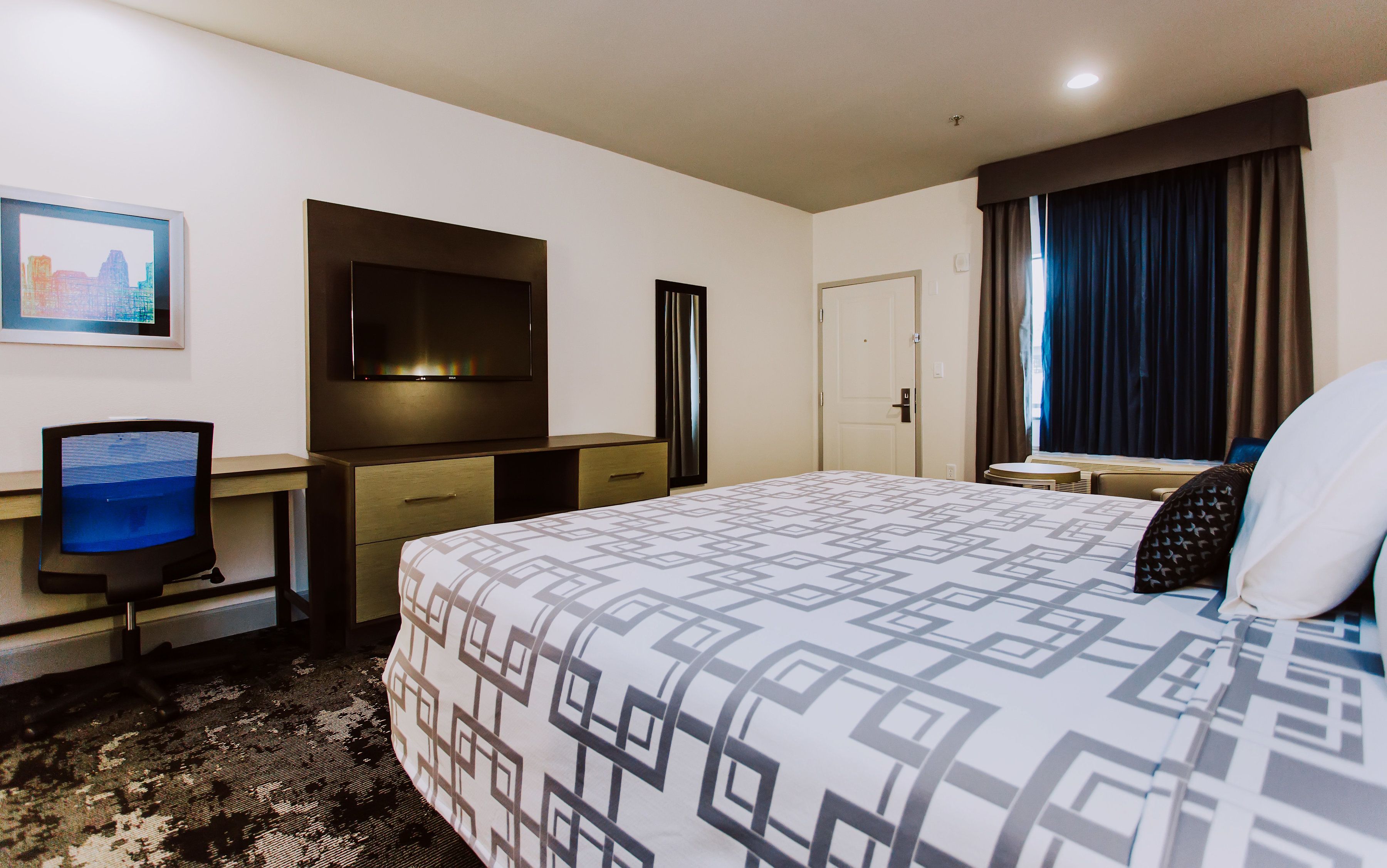 A hotel room with a bed, a desk, a television, and a door.