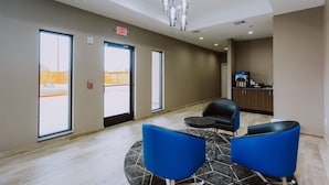 Un hall d’entrée moderne avec deux fauteuils bleus, une petite table et, au fond, un coin cuisine.