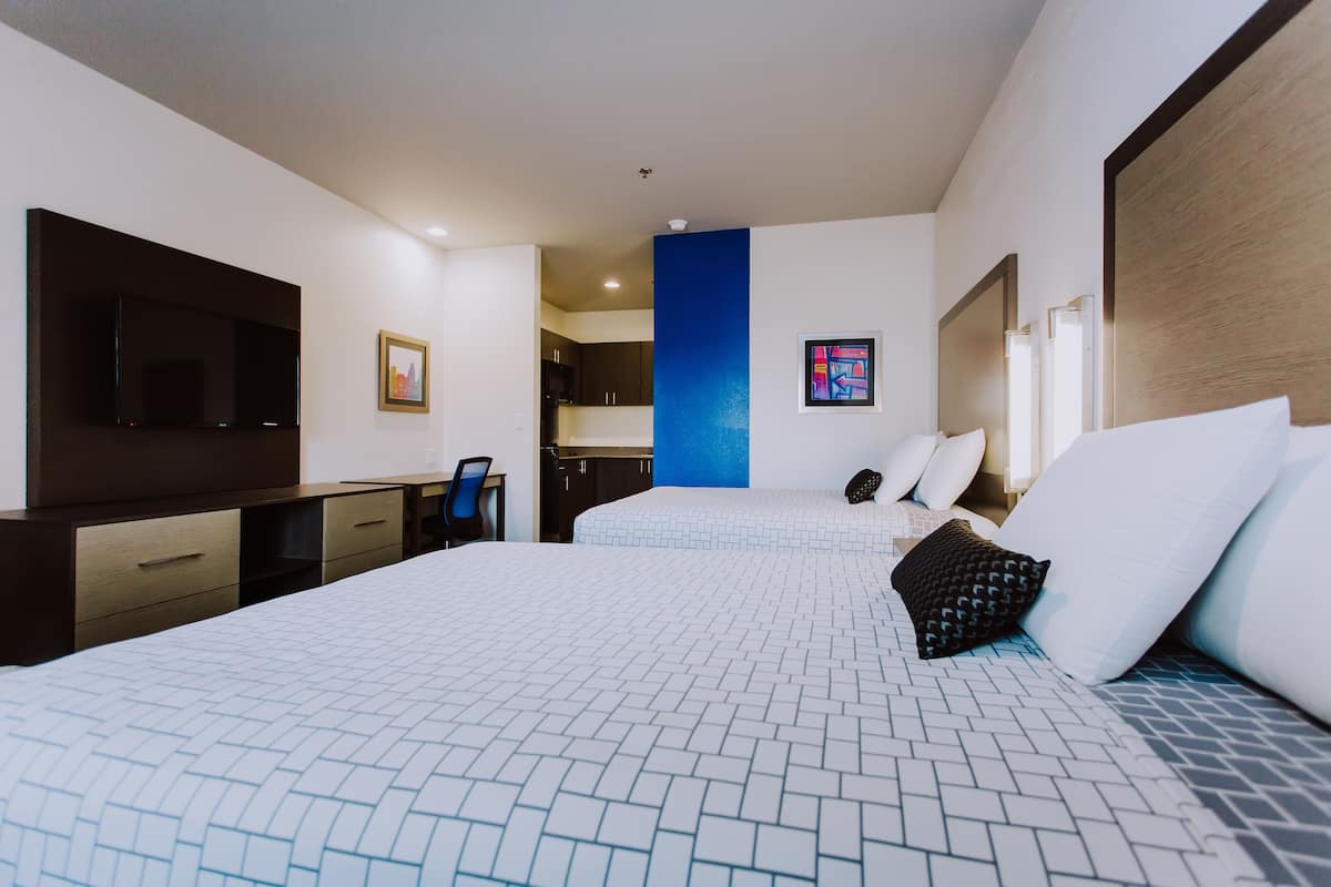 Ein Hotelzimmer mit zwei Betten, einem Fernseher, einem Schreibtisch und einer Küchenzeile.