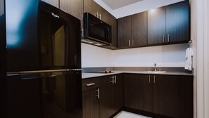 Une cuisine moderne avec des meubles de couleur bois foncé, un réfrigérateur noir et un four à micro-ondes.