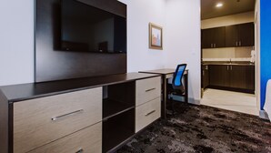 Une chambre d’hôtel moderne dotée d’un téléviseur à écran plat fixé au mur, d’un bureau avec une chaise et d’un coin cuisine.