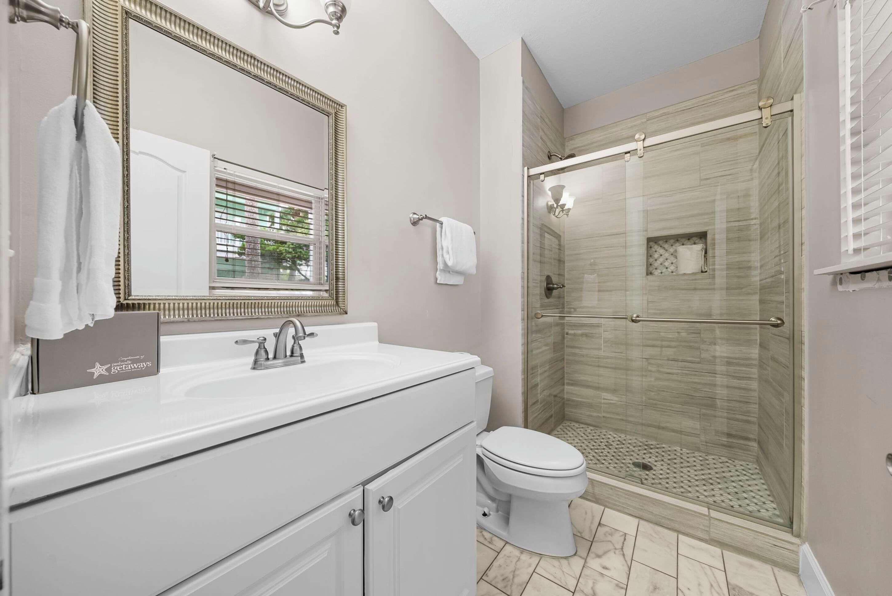 Une salle de bain avec un lavabo blanc, des toilettes, un grand miroir et une douche à parois de verre.
