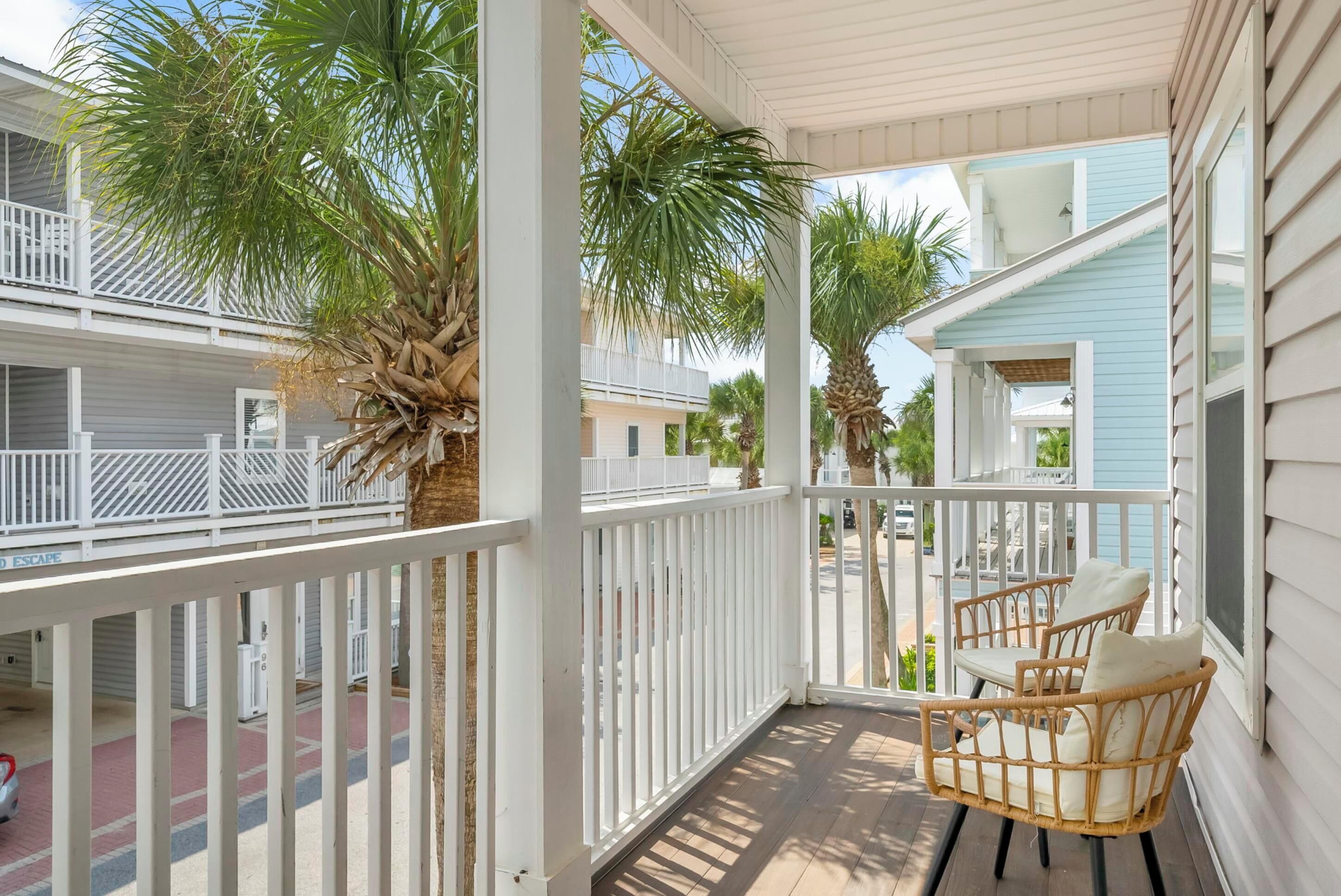 A covered porch with white railings, two wicker chairs, and palm trees.