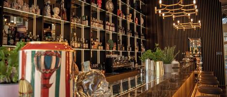 Una zona de bar con estantes llenos de botellas, una encimera de mármol y taburetes.
