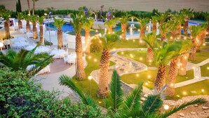 A resort with outdoor seating, palm trees, and a pool area. - UNA HOTELS MH Matera (Borgo Venusio)