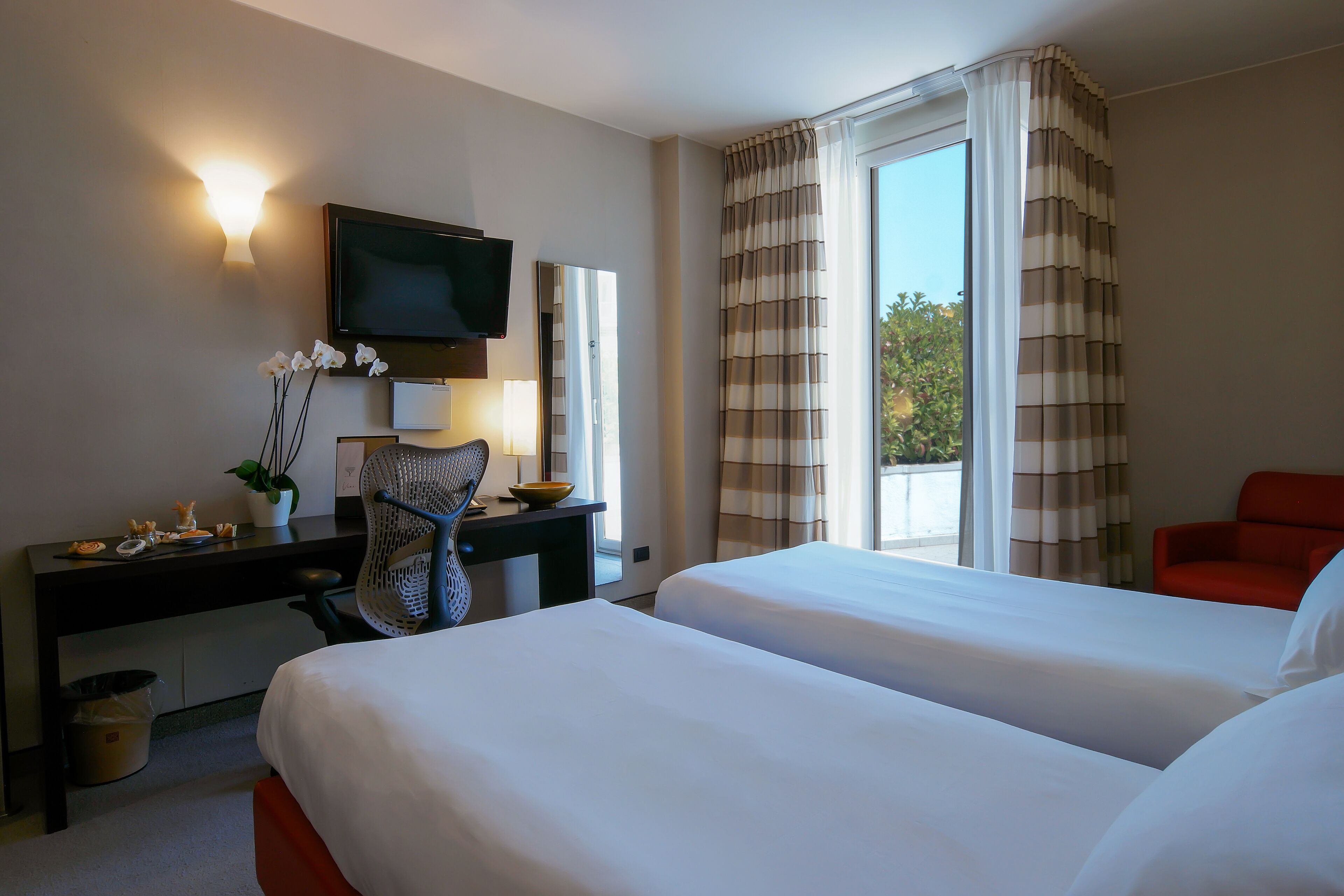Una habitación de hotel con dos camas, un escritorio con una silla, un televisor y una ventana con cortinas.