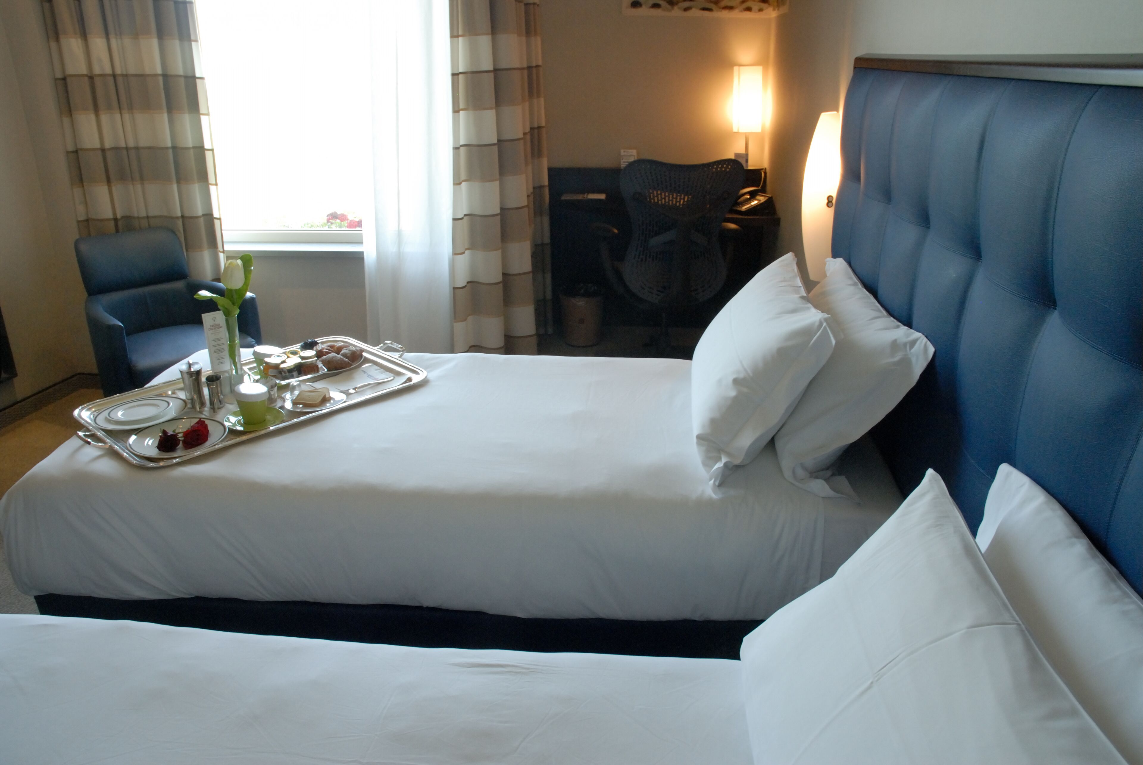 Ein Hotelzimmer mit einem großen Bett, einem Sessel, einem Schreibtisch und einem Tablett mit Speisen und Getränken.