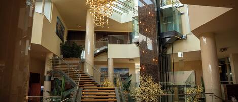 A spacious lobby with a grand staircase, modern chandeliers, and a high ceiling.