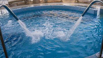 A swimming pool with two water jets, lounge chairs, and a tiled deck area.