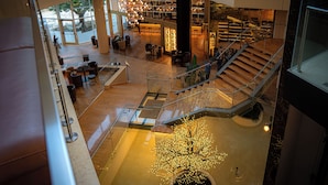 A spacious indoor area with a central staircase, seating areas, and a large illuminated tree sculpture. - UNA HOTELS MH Matera (Borgo Venusio)