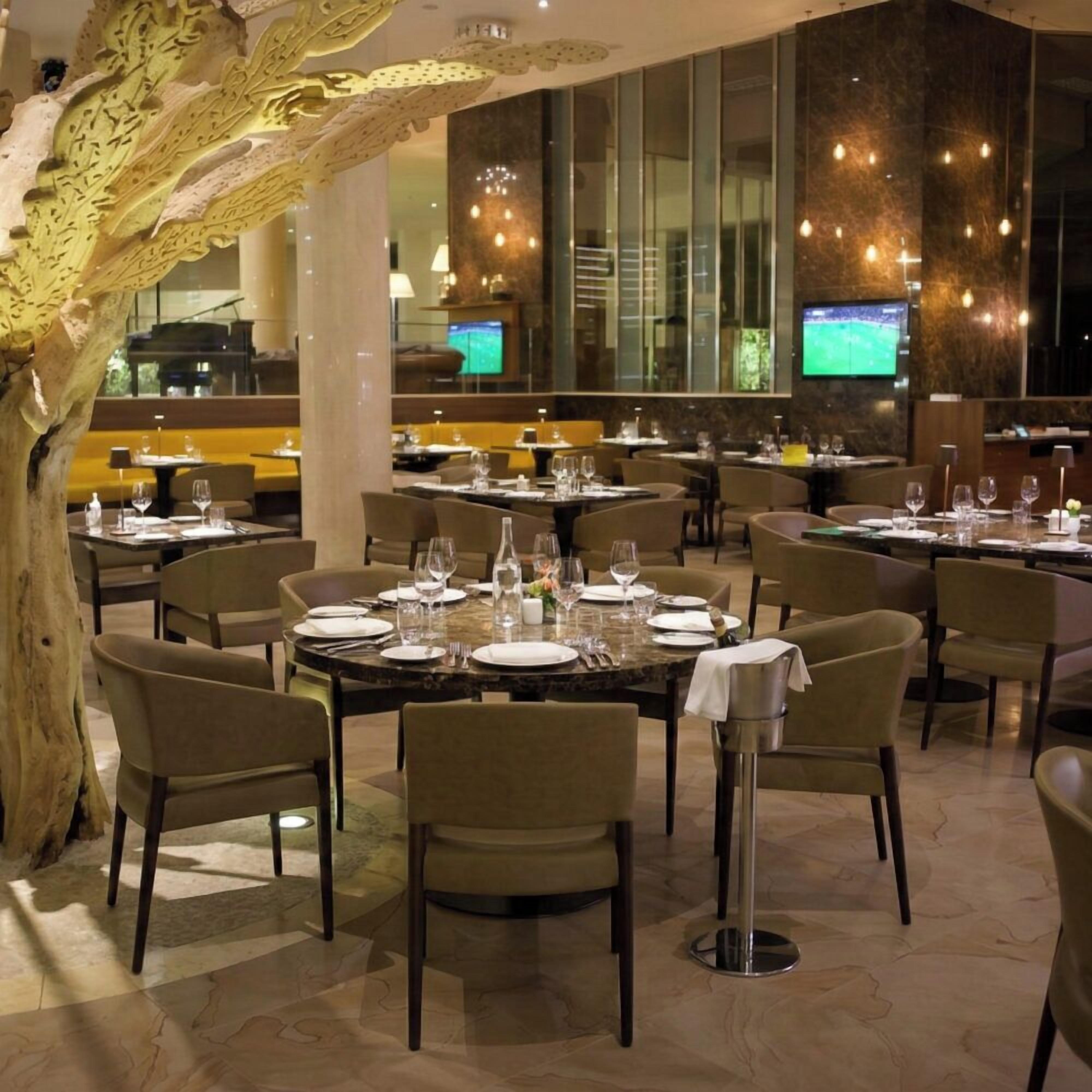 A restaurant with round tables, chairs, and a large tree sculpture.