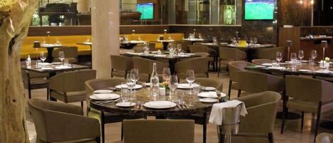 A restaurant with round tables, chairs, and a large tree sculpture.