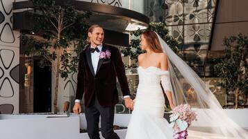 A couple walking hand in hand in front of a modern building with geometric patterns and indoor plants.