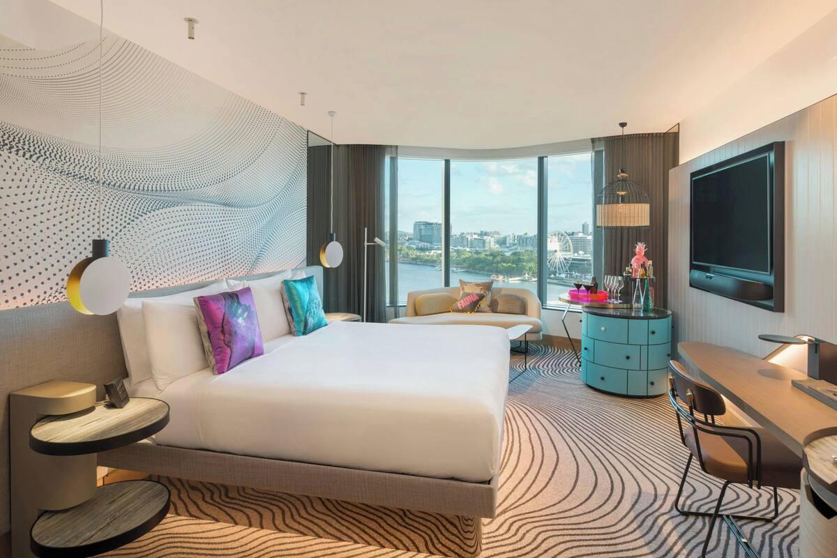Une chambre d’hôtel moderne dotée d’un grand lit, d’un bureau, d’une chaise, d’une télévision et offrant une vue sur la ville.