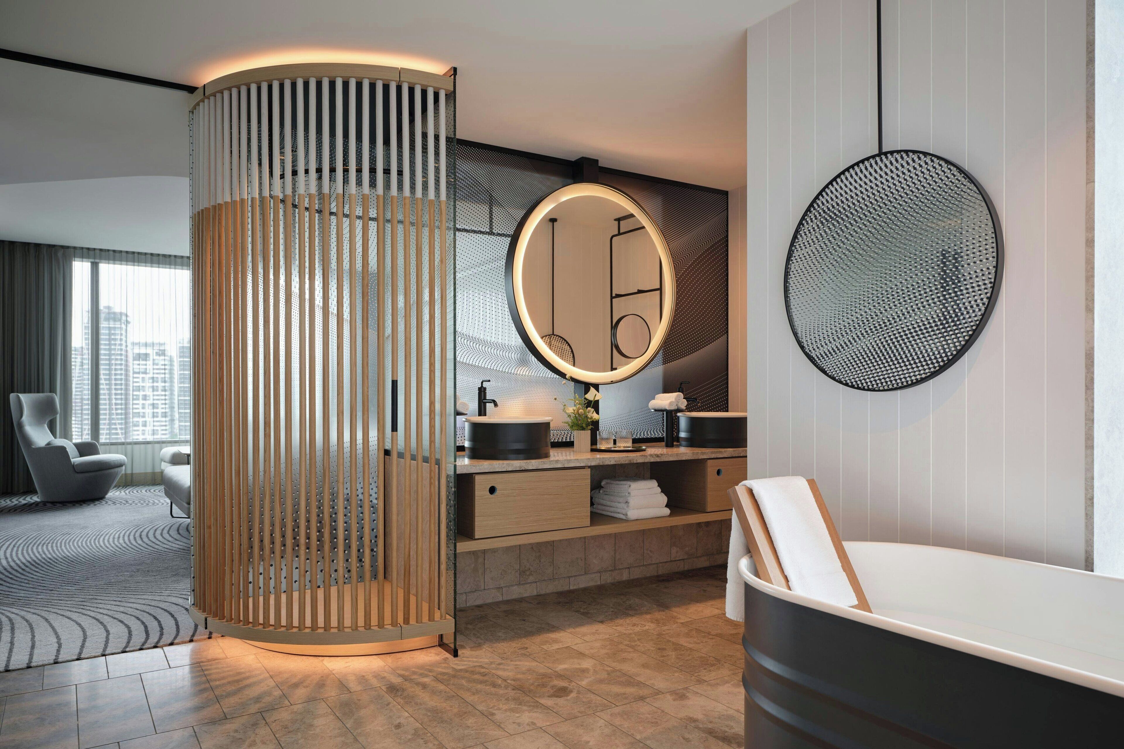 A modern bathroom with a round mirror, a wooden column, and a bathtub.