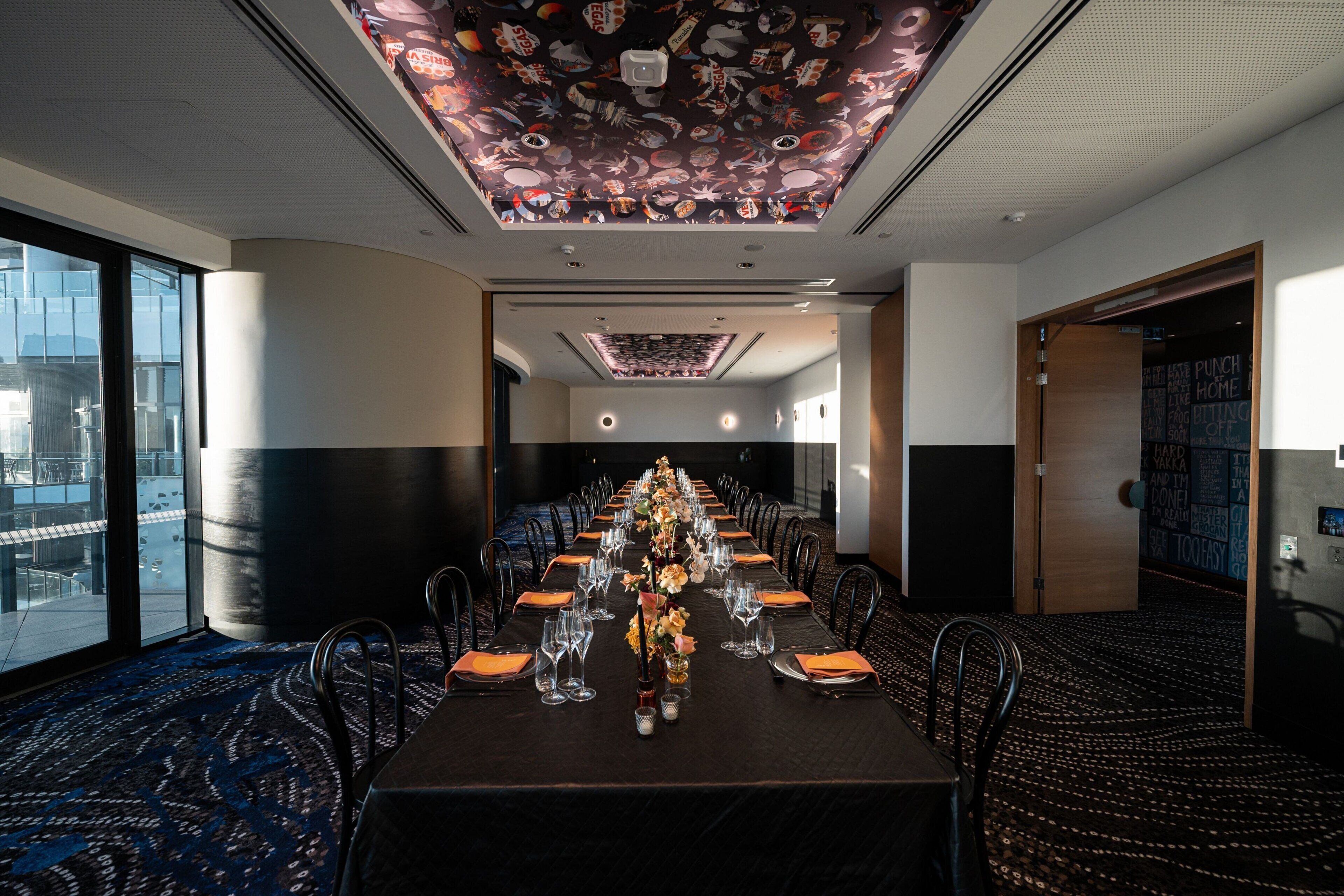 A conference room with a long table set for a meeting, large windows on one side, and a ceiling with a fish-themed design.