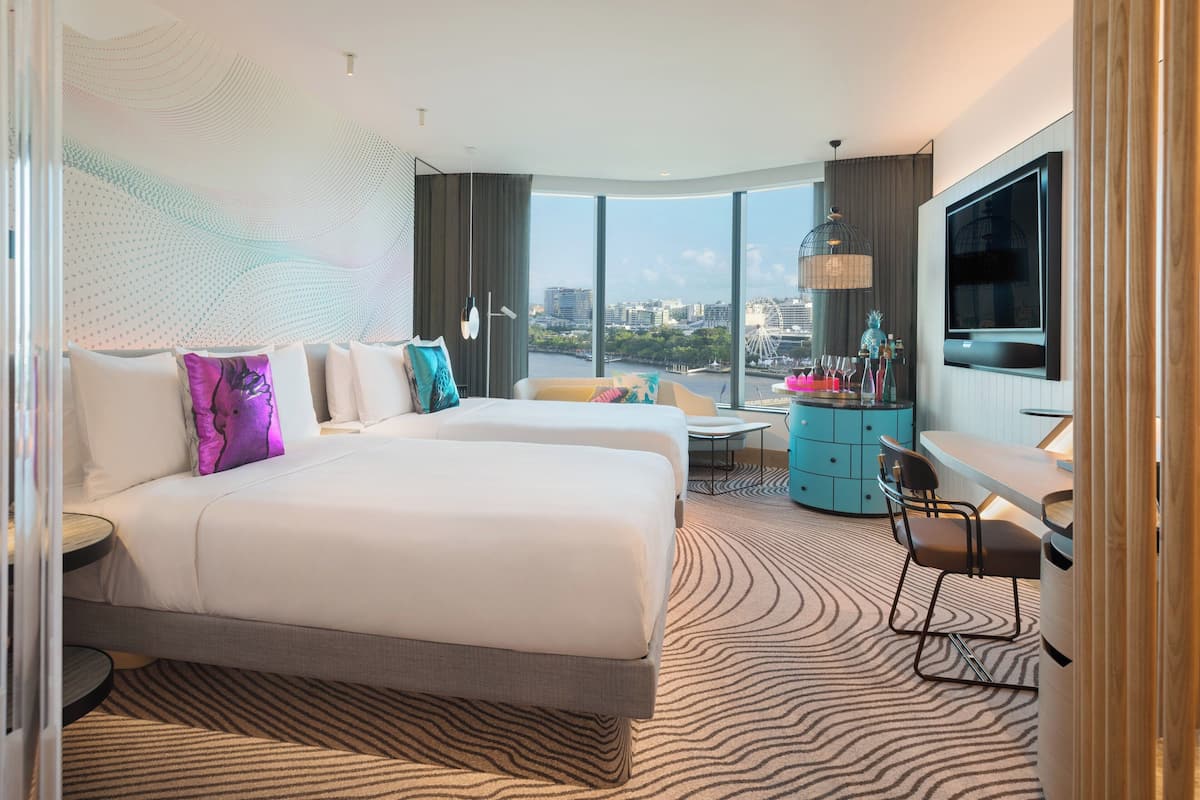 Une chambre d’hôtel moderne avec un grand lit, deux petits lits, un bureau et une télévision.