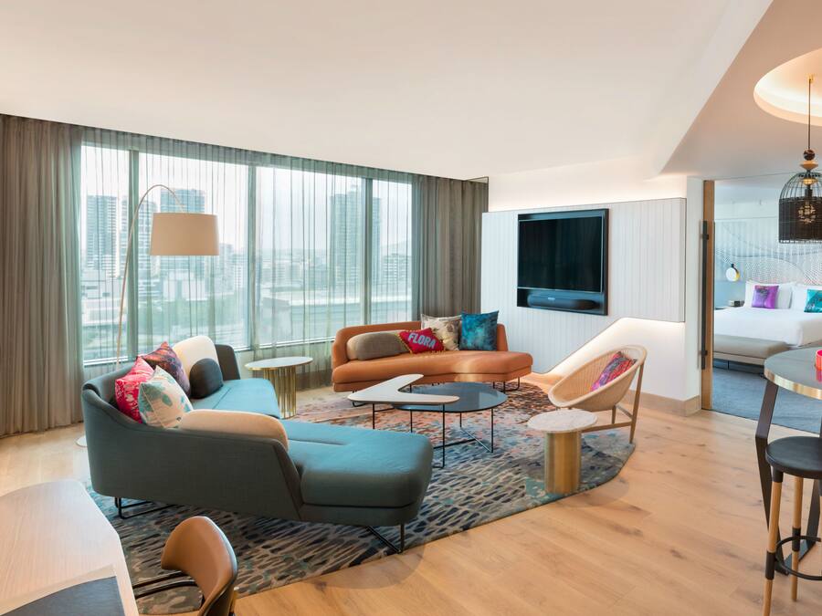 A modern hotel room with a sofa, armchairs, a small table, and a TV.