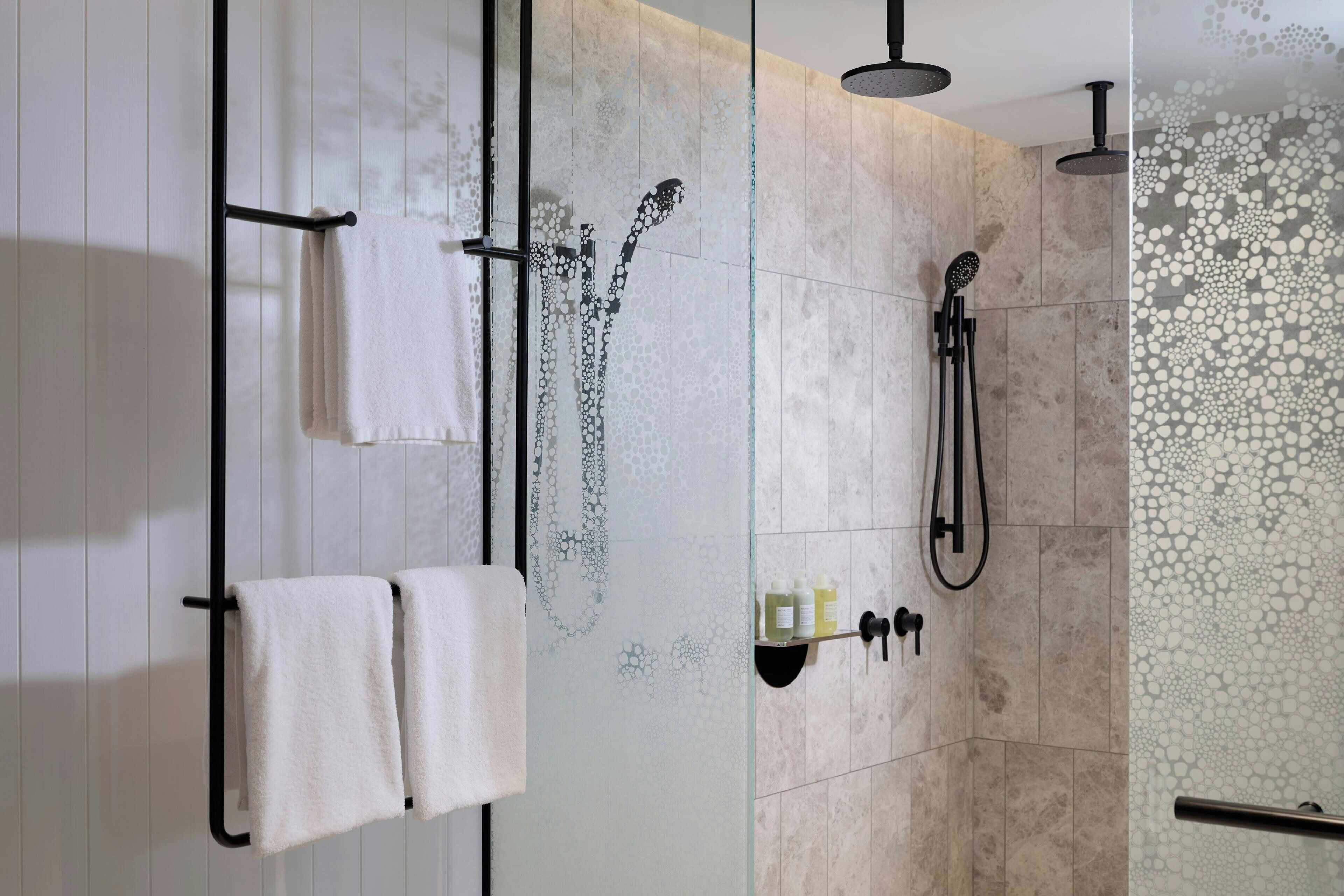 Une salle de bain moderne avec une douche à parois de verre, un porte-serviettes avec deux serviettes et un pommeau de douche.