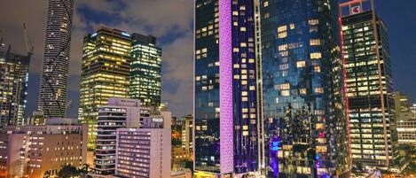 A cityscape at night with modern high-rise buildings, including a prominent building with purple lighting.