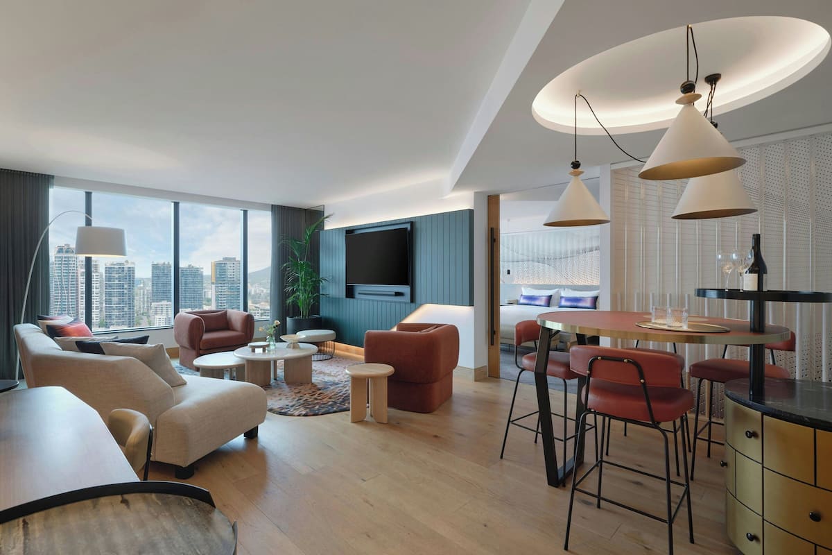 Un salon moderne comprenant un canapé, des fauteuils, un coin repas avec des tabourets de bar et un téléviseur fixé au mur.