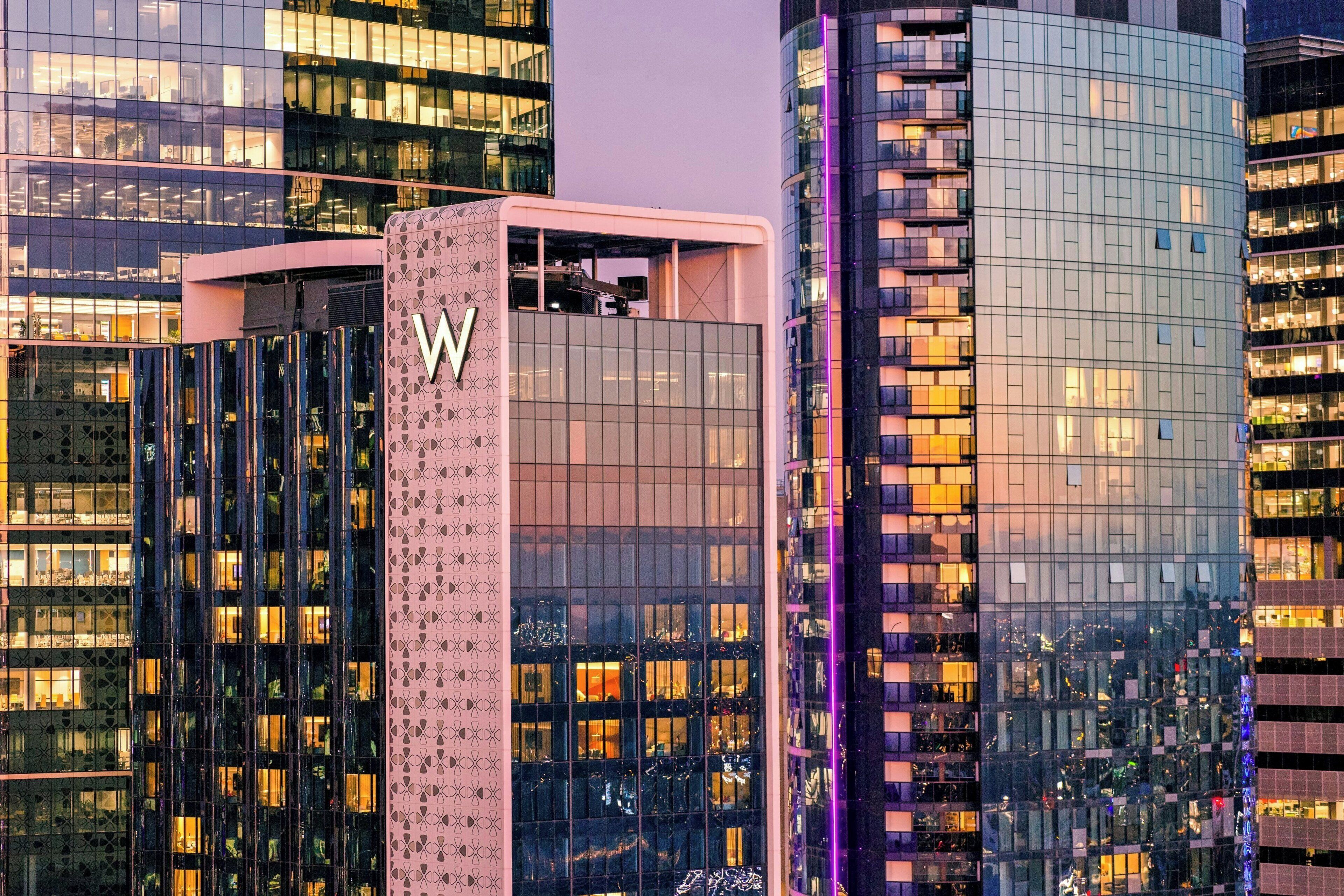 A modern high-rise building with a prominent 'W' logo on the facade, surrounded by other tall buildings with reflective glass windows.