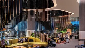 A modern interior with a yellow sofa, round tables, and a staircase with a glass railing.