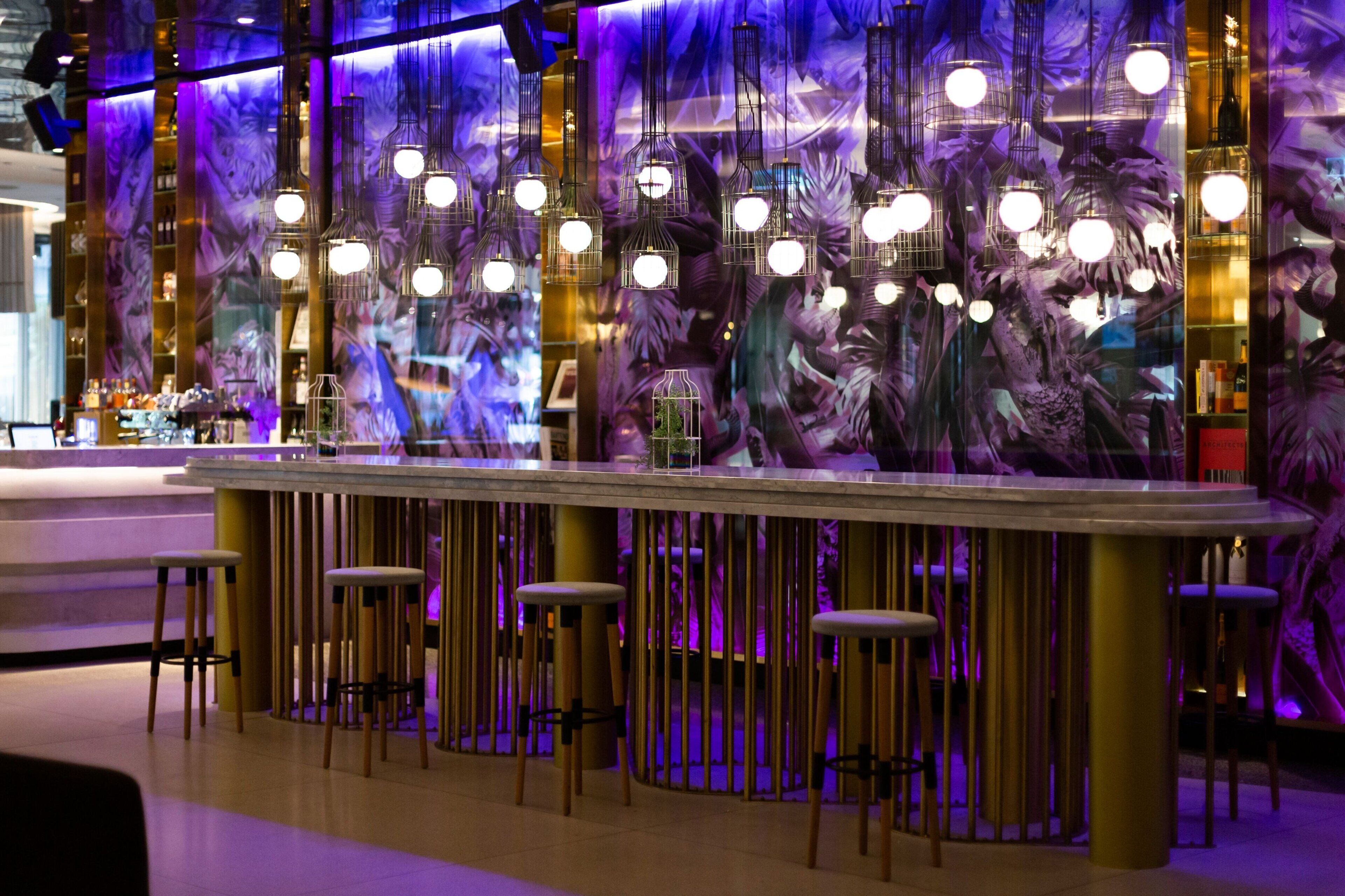 Een bar met een modern design, met een lange bar en krukken en hangende sferische lampen.